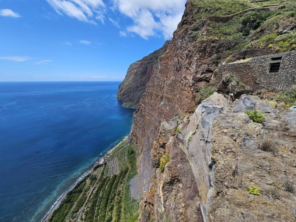 Cruising with Danny and Peter, Holland America Line, Nieuw Statendam, Funchal, Madeira. Portugal, History Adventure | A vibrant collage capturing a day in Funchal, Madeira: a sleek trike navigates winding roads with lush green hills in the background; the panoramic view from Pico dos Barcelos showcases Funchal Bay and the Desertas Islands under a clear sky; Cascata dos Anjos waterfall cascades from cliffs onto a road, surrounded by verdant greenery; Praia da Madalena do Mar’s pebbled beach and black volcanic sand meet gentle waves with towering cliffs above; the misty Valley of the Nuns nestles between rugged mountains, dotted with stone houses and chestnut groves; Cabo Girão’s glass-bottomed skywalk reveals a dizzying drop to the Atlantic and terraced fields below; a plate of warm bolo do caco flatbread filled with steak sits on a café table in Funchal’s colorful old town; the CR7 Museum displays Cristiano Ronaldo’s trophies and jerseys with a waterfront view of the Nieuw Statendam; and Nami Sushi Bar’s elegant sushi platter gleams under soft lighting aboard the ship.
