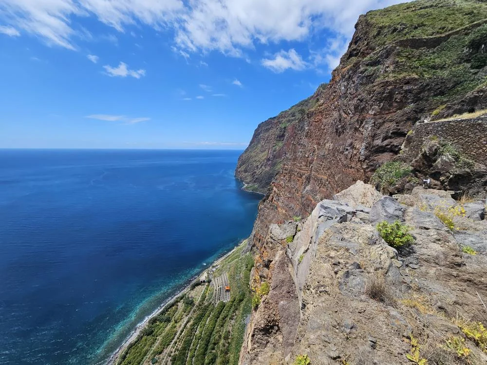 Cruising with Danny and Peter, Holland America Line, Nieuw Statendam, Funchal, Madeira. Portugal, History Adventure | A vibrant collage capturing a day in Funchal, Madeira: a sleek trike navigates winding roads with lush green hills in the background; the panoramic view from Pico dos Barcelos showcases Funchal Bay and the Desertas Islands under a clear sky; Cascata dos Anjos waterfall cascades from cliffs onto a road, surrounded by verdant greenery; Praia da Madalena do Mar’s pebbled beach and black volcanic sand meet gentle waves with towering cliffs above; the misty Valley of the Nuns nestles between rugged mountains, dotted with stone houses and chestnut groves; Cabo Girão’s glass-bottomed skywalk reveals a dizzying drop to the Atlantic and terraced fields below; a plate of warm bolo do caco flatbread filled with steak sits on a café table in Funchal’s colorful old town; the CR7 Museum displays Cristiano Ronaldo’s trophies and jerseys with a waterfront view of the Nieuw Statendam; and Nami Sushi Bar’s elegant sushi platter gleams under soft lighting aboard the ship.
