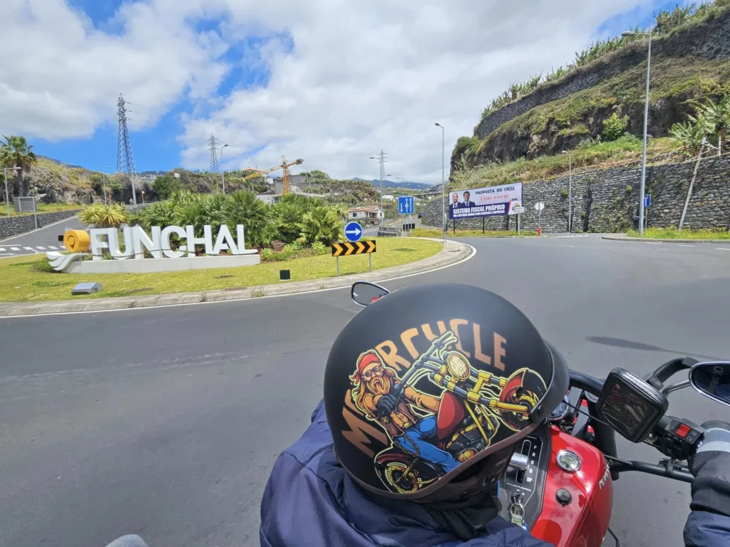Cruising with Danny and Peter, Holland America Line, Nieuw Statendam, Funchal, Madeira. Portugal, History Adventure | A vibrant collage capturing a day in Funchal, Madeira: a sleek trike navigates winding roads with lush green hills in the background; the panoramic view from Pico dos Barcelos showcases Funchal Bay and the Desertas Islands under a clear sky; Cascata dos Anjos waterfall cascades from cliffs onto a road, surrounded by verdant greenery; Praia da Madalena do Mar’s pebbled beach and black volcanic sand meet gentle waves with towering cliffs above; the misty Valley of the Nuns nestles between rugged mountains, dotted with stone houses and chestnut groves; Cabo Girão’s glass-bottomed skywalk reveals a dizzying drop to the Atlantic and terraced fields below; a plate of warm bolo do caco flatbread filled with steak sits on a café table in Funchal’s colorful old town; the CR7 Museum displays Cristiano Ronaldo’s trophies and jerseys with a waterfront view of the Nieuw Statendam; and Nami Sushi Bar’s elegant sushi platter gleams under soft lighting aboard the ship.