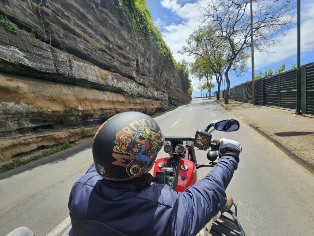 Cruising with Danny and Peter, Holland America Line, Nieuw Statendam, Funchal, Madeira. Portugal, History Adventure | A vibrant collage capturing a day in Funchal, Madeira: a sleek trike navigates winding roads with lush green hills in the background; the panoramic view from Pico dos Barcelos showcases Funchal Bay and the Desertas Islands under a clear sky; Cascata dos Anjos waterfall cascades from cliffs onto a road, surrounded by verdant greenery; Praia da Madalena do Mar’s pebbled beach and black volcanic sand meet gentle waves with towering cliffs above; the misty Valley of the Nuns nestles between rugged mountains, dotted with stone houses and chestnut groves; Cabo Girão’s glass-bottomed skywalk reveals a dizzying drop to the Atlantic and terraced fields below; a plate of warm bolo do caco flatbread filled with steak sits on a café table in Funchal’s colorful old town; the CR7 Museum displays Cristiano Ronaldo’s trophies and jerseys with a waterfront view of the Nieuw Statendam; and Nami Sushi Bar’s elegant sushi platter gleams under soft lighting aboard the ship.