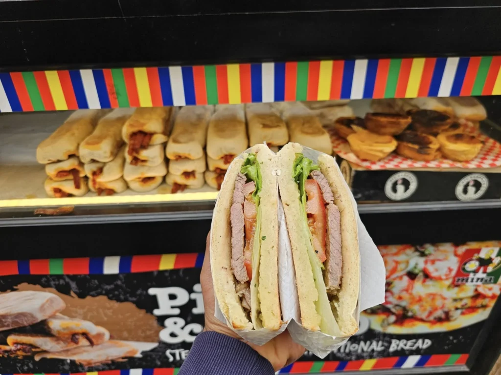 Cruising with Danny and Peter, Holland America Line, Nieuw Statendam, Funchal, Madeira. Portugal, History Adventure | A vibrant collage capturing a day in Funchal, Madeira: a sleek trike navigates winding roads with lush green hills in the background; the panoramic view from Pico dos Barcelos showcases Funchal Bay and the Desertas Islands under a clear sky; Cascata dos Anjos waterfall cascades from cliffs onto a road, surrounded by verdant greenery; Praia da Madalena do Mar’s pebbled beach and black volcanic sand meet gentle waves with towering cliffs above; the misty Valley of the Nuns nestles between rugged mountains, dotted with stone houses and chestnut groves; Cabo Girão’s glass-bottomed skywalk reveals a dizzying drop to the Atlantic and terraced fields below; a plate of warm bolo do caco flatbread filled with steak sits on a café table in Funchal’s colorful old town; the CR7 Museum displays Cristiano Ronaldo’s trophies and jerseys with a waterfront view of the Nieuw Statendam; and Nami Sushi Bar’s elegant sushi platter gleams under soft lighting aboard the ship.