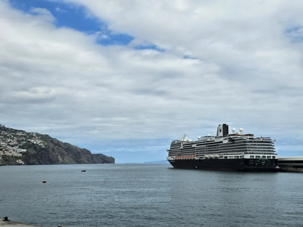 Cruising with Danny and Peter, Holland America Line, Nieuw Statendam, Funchal, Madeira. Portugal, History Adventure | A vibrant collage capturing a day in Funchal, Madeira: a sleek trike navigates winding roads with lush green hills in the background; the panoramic view from Pico dos Barcelos showcases Funchal Bay and the Desertas Islands under a clear sky; Cascata dos Anjos waterfall cascades from cliffs onto a road, surrounded by verdant greenery; Praia da Madalena do Mar’s pebbled beach and black volcanic sand meet gentle waves with towering cliffs above; the misty Valley of the Nuns nestles between rugged mountains, dotted with stone houses and chestnut groves; Cabo Girão’s glass-bottomed skywalk reveals a dizzying drop to the Atlantic and terraced fields below; a plate of warm bolo do caco flatbread filled with steak sits on a café table in Funchal’s colorful old town; the CR7 Museum displays Cristiano Ronaldo’s trophies and jerseys with a waterfront view of the Nieuw Statendam; and Nami Sushi Bar’s elegant sushi platter gleams under soft lighting aboard the ship.