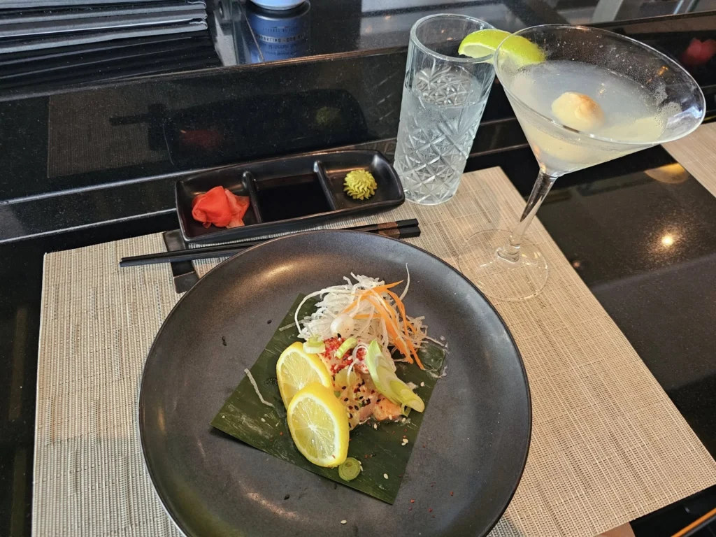 Cruising with Danny and Peter, Holland America Line, Nieuw Statendam, Funchal, Madeira. Portugal, History Adventure | A vibrant collage capturing a day in Funchal, Madeira: a sleek trike navigates winding roads with lush green hills in the background; the panoramic view from Pico dos Barcelos showcases Funchal Bay and the Desertas Islands under a clear sky; Cascata dos Anjos waterfall cascades from cliffs onto a road, surrounded by verdant greenery; Praia da Madalena do Mar’s pebbled beach and black volcanic sand meet gentle waves with towering cliffs above; the misty Valley of the Nuns nestles between rugged mountains, dotted with stone houses and chestnut groves; Cabo Girão’s glass-bottomed skywalk reveals a dizzying drop to the Atlantic and terraced fields below; a plate of warm bolo do caco flatbread filled with steak sits on a café table in Funchal’s colorful old town; the CR7 Museum displays Cristiano Ronaldo’s trophies and jerseys with a waterfront view of the Nieuw Statendam; and Nami Sushi Bar’s elegant sushi platter gleams under soft lighting aboard the ship.