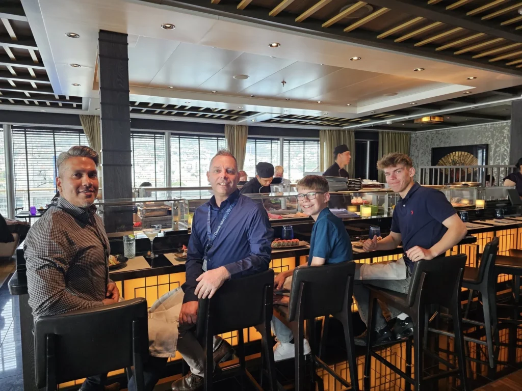 Cruising with Danny and Peter, Holland America Line, Nieuw Statendam, Funchal, Madeira. Portugal, History Adventure | A vibrant collage capturing a day in Funchal, Madeira: a sleek trike navigates winding roads with lush green hills in the background; the panoramic view from Pico dos Barcelos showcases Funchal Bay and the Desertas Islands under a clear sky; Cascata dos Anjos waterfall cascades from cliffs onto a road, surrounded by verdant greenery; Praia da Madalena do Mar’s pebbled beach and black volcanic sand meet gentle waves with towering cliffs above; the misty Valley of the Nuns nestles between rugged mountains, dotted with stone houses and chestnut groves; Cabo Girão’s glass-bottomed skywalk reveals a dizzying drop to the Atlantic and terraced fields below; a plate of warm bolo do caco flatbread filled with steak sits on a café table in Funchal’s colorful old town; the CR7 Museum displays Cristiano Ronaldo’s trophies and jerseys with a waterfront view of the Nieuw Statendam; and Nami Sushi Bar’s elegant sushi platter gleams under soft lighting aboard the ship.