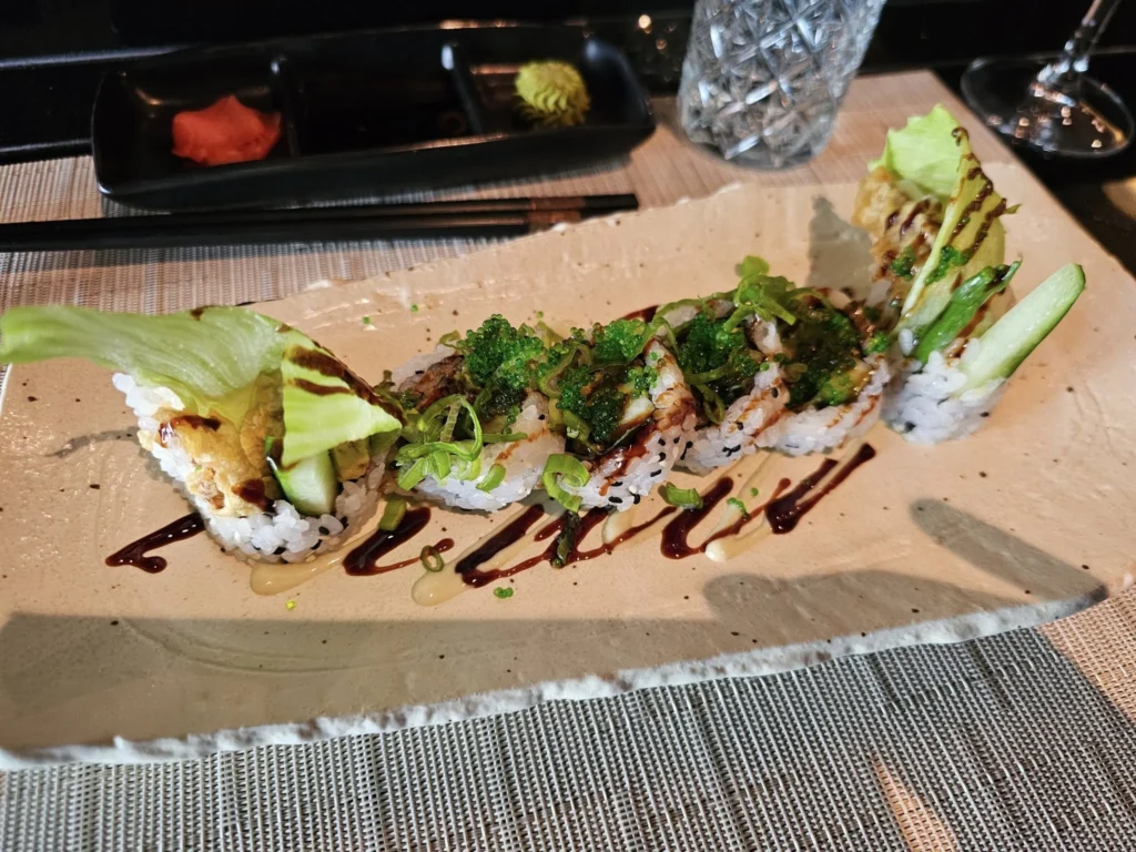 Cruising with Danny and Peter, Holland America Line, Nieuw Statendam, Funchal, Madeira. Portugal, History Adventure | A vibrant collage capturing a day in Funchal, Madeira: a sleek trike navigates winding roads with lush green hills in the background; the panoramic view from Pico dos Barcelos showcases Funchal Bay and the Desertas Islands under a clear sky; Cascata dos Anjos waterfall cascades from cliffs onto a road, surrounded by verdant greenery; Praia da Madalena do Mar’s pebbled beach and black volcanic sand meet gentle waves with towering cliffs above; the misty Valley of the Nuns nestles between rugged mountains, dotted with stone houses and chestnut groves; Cabo Girão’s glass-bottomed skywalk reveals a dizzying drop to the Atlantic and terraced fields below; a plate of warm bolo do caco flatbread filled with steak sits on a café table in Funchal’s colorful old town; the CR7 Museum displays Cristiano Ronaldo’s trophies and jerseys with a waterfront view of the Nieuw Statendam; and Nami Sushi Bar’s elegant sushi platter gleams under soft lighting aboard the ship.