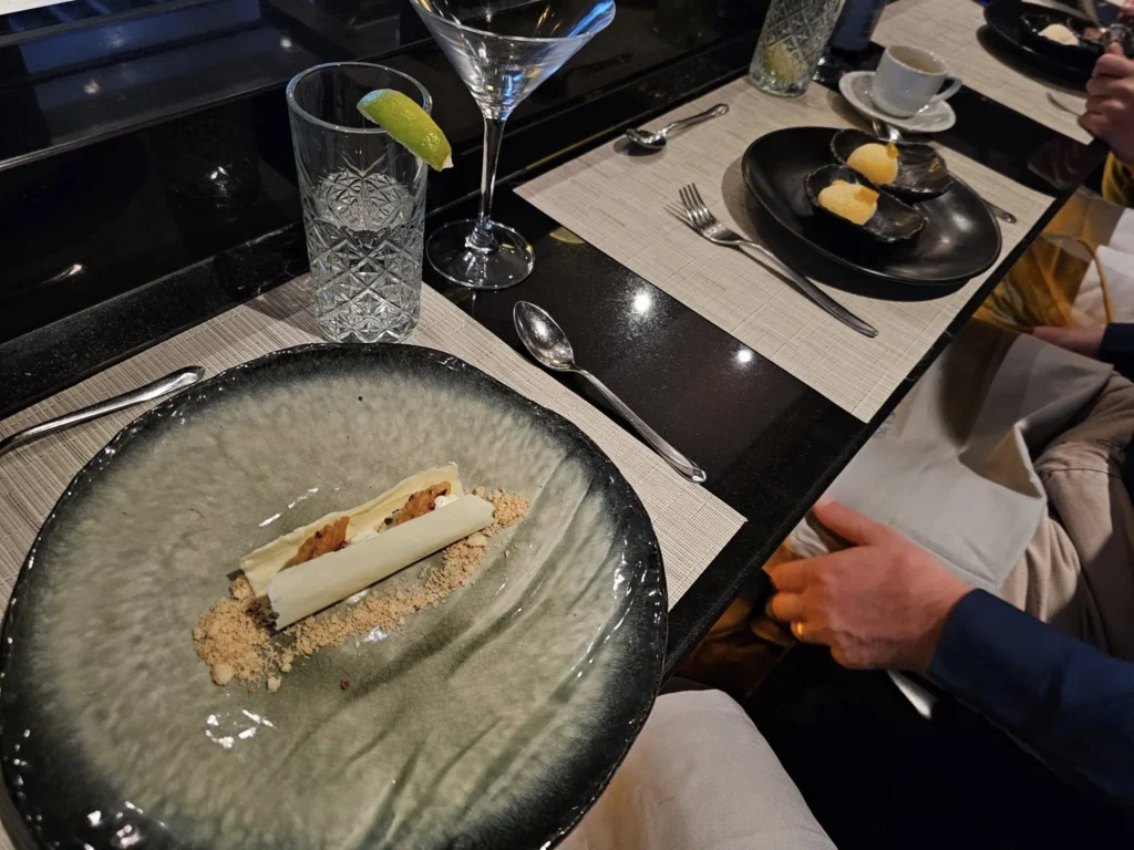 Cruising with Danny and Peter, Holland America Line, Nieuw Statendam, Funchal, Madeira. Portugal, History Adventure | A vibrant collage capturing a day in Funchal, Madeira: a sleek trike navigates winding roads with lush green hills in the background; the panoramic view from Pico dos Barcelos showcases Funchal Bay and the Desertas Islands under a clear sky; Cascata dos Anjos waterfall cascades from cliffs onto a road, surrounded by verdant greenery; Praia da Madalena do Mar’s pebbled beach and black volcanic sand meet gentle waves with towering cliffs above; the misty Valley of the Nuns nestles between rugged mountains, dotted with stone houses and chestnut groves; Cabo Girão’s glass-bottomed skywalk reveals a dizzying drop to the Atlantic and terraced fields below; a plate of warm bolo do caco flatbread filled with steak sits on a café table in Funchal’s colorful old town; the CR7 Museum displays Cristiano Ronaldo’s trophies and jerseys with a waterfront view of the Nieuw Statendam; and Nami Sushi Bar’s elegant sushi platter gleams under soft lighting aboard the ship.