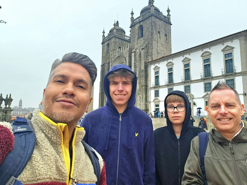 Cruising with Danny and Peter, Holland America Line, Nieuw Statendam, Leixoes, Porto, Portugal, Rainy Adventure | A vibrant collage capturing a rainy day adventure in Porto, Portugal, from the Holland America Line’s Nieuw Statendam cruise. The scene includes a colorful tuk-tuk navigating Porto’s wet, cobblestone streets with historic buildings in the background, the iconic Dom Luís I Bridge spanning the Douro River under gray skies, the majestic Porto Cathedral with its Gothic facade glistening in the rain, and the intricate blue-and-white azulejo tiles of São Bento Station’s atrium. Onboard, a beautifully plated dish from Tamarind restaurant showcases exotic flavors, while the lively Lido Fun Fair on the Lido Midship deck features children enjoying carnival games under a retractable roof, with colorful decorations and cotton candy adding festive cheer.