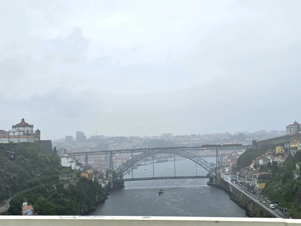 Cruising with Danny and Peter, Holland America Line, Nieuw Statendam, Leixoes, Porto, Portugal, Rainy Adventure | A vibrant collage capturing a rainy day adventure in Porto, Portugal, from the Holland America Line’s Nieuw Statendam cruise. The scene includes a colorful tuk-tuk navigating Porto’s wet, cobblestone streets with historic buildings in the background, the iconic Dom Luís I Bridge spanning the Douro River under gray skies, the majestic Porto Cathedral with its Gothic facade glistening in the rain, and the intricate blue-and-white azulejo tiles of São Bento Station’s atrium. Onboard, a beautifully plated dish from Tamarind restaurant showcases exotic flavors, while the lively Lido Fun Fair on the Lido Midship deck features children enjoying carnival games under a retractable roof, with colorful decorations and cotton candy adding festive cheer.