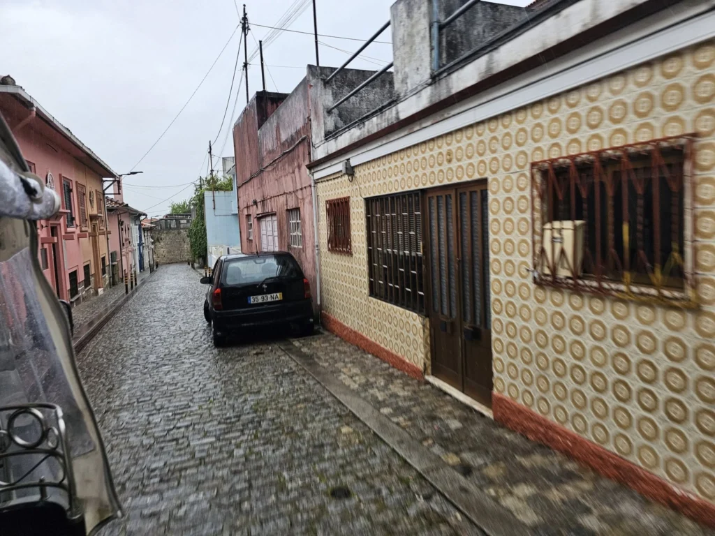 Cruising with Danny and Peter, Holland America Line, Nieuw Statendam, Leixoes, Porto, Portugal, Rainy Adventure | A vibrant collage capturing a rainy day adventure in Porto, Portugal, from the Holland America Line’s Nieuw Statendam cruise. The scene includes a colorful tuk-tuk navigating Porto’s wet, cobblestone streets with historic buildings in the background, the iconic Dom Luís I Bridge spanning the Douro River under gray skies, the majestic Porto Cathedral with its Gothic facade glistening in the rain, and the intricate blue-and-white azulejo tiles of São Bento Station’s atrium. Onboard, a beautifully plated dish from Tamarind restaurant showcases exotic flavors, while the lively Lido Fun Fair on the Lido Midship deck features children enjoying carnival games under a retractable roof, with colorful decorations and cotton candy adding festive cheer.