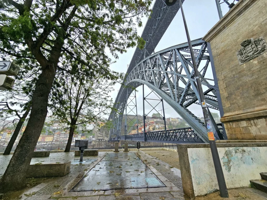 Cruising with Danny and Peter, Holland America Line, Nieuw Statendam, Leixoes, Porto, Portugal, Rainy Adventure | A vibrant collage capturing a rainy day adventure in Porto, Portugal, from the Holland America Line’s Nieuw Statendam cruise. The scene includes a colorful tuk-tuk navigating Porto’s wet, cobblestone streets with historic buildings in the background, the iconic Dom Luís I Bridge spanning the Douro River under gray skies, the majestic Porto Cathedral with its Gothic facade glistening in the rain, and the intricate blue-and-white azulejo tiles of São Bento Station’s atrium. Onboard, a beautifully plated dish from Tamarind restaurant showcases exotic flavors, while the lively Lido Fun Fair on the Lido Midship deck features children enjoying carnival games under a retractable roof, with colorful decorations and cotton candy adding festive cheer.