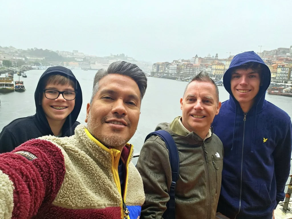 Cruising with Danny and Peter, Holland America Line, Nieuw Statendam, Leixoes, Porto, Portugal, Rainy Adventure | A vibrant collage capturing a rainy day adventure in Porto, Portugal, from the Holland America Line’s Nieuw Statendam cruise. The scene includes a colorful tuk-tuk navigating Porto’s wet, cobblestone streets with historic buildings in the background, the iconic Dom Luís I Bridge spanning the Douro River under gray skies, the majestic Porto Cathedral with its Gothic facade glistening in the rain, and the intricate blue-and-white azulejo tiles of São Bento Station’s atrium. Onboard, a beautifully plated dish from Tamarind restaurant showcases exotic flavors, while the lively Lido Fun Fair on the Lido Midship deck features children enjoying carnival games under a retractable roof, with colorful decorations and cotton candy adding festive cheer.