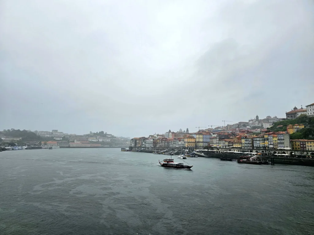 Cruising with Danny and Peter, Holland America Line, Nieuw Statendam, Leixoes, Porto, Portugal, Rainy Adventure | A vibrant collage capturing a rainy day adventure in Porto, Portugal, from the Holland America Line’s Nieuw Statendam cruise. The scene includes a colorful tuk-tuk navigating Porto’s wet, cobblestone streets with historic buildings in the background, the iconic Dom Luís I Bridge spanning the Douro River under gray skies, the majestic Porto Cathedral with its Gothic facade glistening in the rain, and the intricate blue-and-white azulejo tiles of São Bento Station’s atrium. Onboard, a beautifully plated dish from Tamarind restaurant showcases exotic flavors, while the lively Lido Fun Fair on the Lido Midship deck features children enjoying carnival games under a retractable roof, with colorful decorations and cotton candy adding festive cheer.