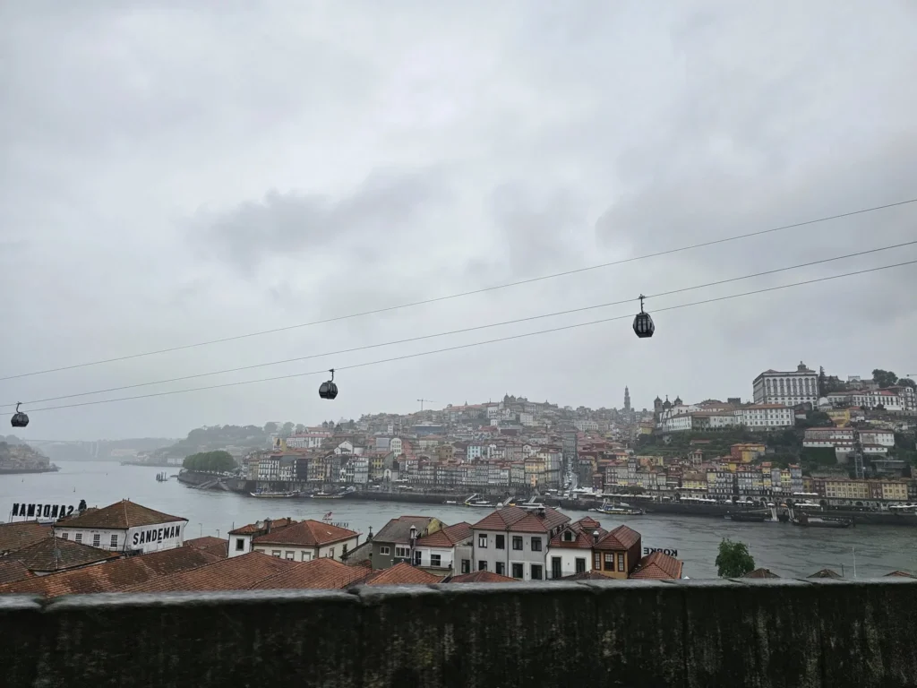 Cruising with Danny and Peter, Holland America Line, Nieuw Statendam, Leixoes, Porto, Portugal, Rainy Adventure | A vibrant collage capturing a rainy day adventure in Porto, Portugal, from the Holland America Line’s Nieuw Statendam cruise. The scene includes a colorful tuk-tuk navigating Porto’s wet, cobblestone streets with historic buildings in the background, the iconic Dom Luís I Bridge spanning the Douro River under gray skies, the majestic Porto Cathedral with its Gothic facade glistening in the rain, and the intricate blue-and-white azulejo tiles of São Bento Station’s atrium. Onboard, a beautifully plated dish from Tamarind restaurant showcases exotic flavors, while the lively Lido Fun Fair on the Lido Midship deck features children enjoying carnival games under a retractable roof, with colorful decorations and cotton candy adding festive cheer.