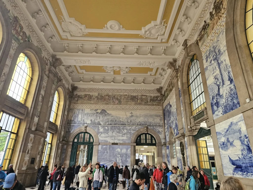 Cruising with Danny and Peter, Holland America Line, Nieuw Statendam, Leixoes, Porto, Portugal, Rainy Adventure | A vibrant collage capturing a rainy day adventure in Porto, Portugal, from the Holland America Line’s Nieuw Statendam cruise. The scene includes a colorful tuk-tuk navigating Porto’s wet, cobblestone streets with historic buildings in the background, the iconic Dom Luís I Bridge spanning the Douro River under gray skies, the majestic Porto Cathedral with its Gothic facade glistening in the rain, and the intricate blue-and-white azulejo tiles of São Bento Station’s atrium. Onboard, a beautifully plated dish from Tamarind restaurant showcases exotic flavors, while the lively Lido Fun Fair on the Lido Midship deck features children enjoying carnival games under a retractable roof, with colorful decorations and cotton candy adding festive cheer.