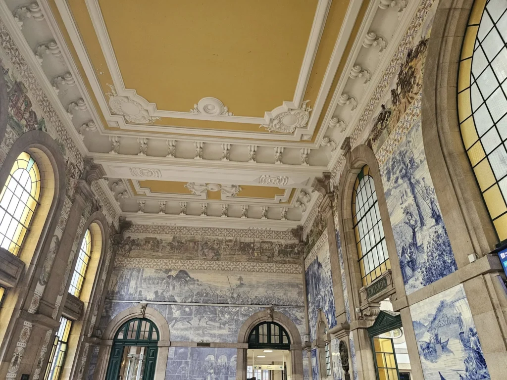 Cruising with Danny and Peter, Holland America Line, Nieuw Statendam, Leixoes, Porto, Portugal, Rainy Adventure | A vibrant collage capturing a rainy day adventure in Porto, Portugal, from the Holland America Line’s Nieuw Statendam cruise. The scene includes a colorful tuk-tuk navigating Porto’s wet, cobblestone streets with historic buildings in the background, the iconic Dom Luís I Bridge spanning the Douro River under gray skies, the majestic Porto Cathedral with its Gothic facade glistening in the rain, and the intricate blue-and-white azulejo tiles of São Bento Station’s atrium. Onboard, a beautifully plated dish from Tamarind restaurant showcases exotic flavors, while the lively Lido Fun Fair on the Lido Midship deck features children enjoying carnival games under a retractable roof, with colorful decorations and cotton candy adding festive cheer.