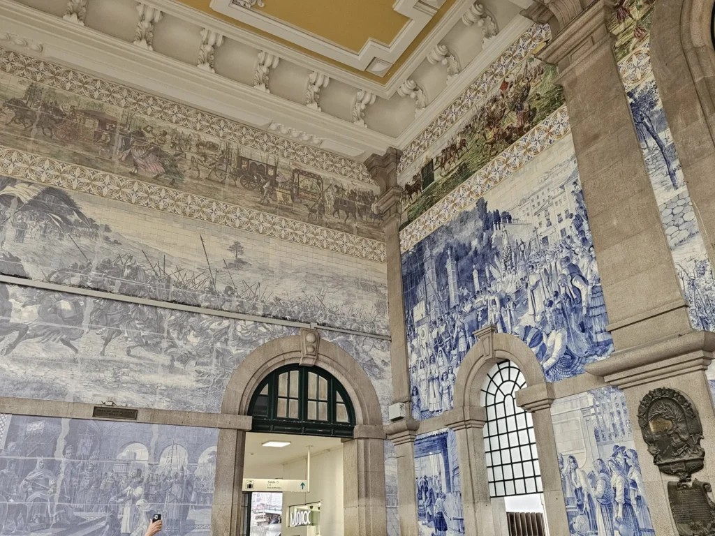 Cruising with Danny and Peter, Holland America Line, Nieuw Statendam, Leixoes, Porto, Portugal, Rainy Adventure | A vibrant collage capturing a rainy day adventure in Porto, Portugal, from the Holland America Line’s Nieuw Statendam cruise. The scene includes a colorful tuk-tuk navigating Porto’s wet, cobblestone streets with historic buildings in the background, the iconic Dom Luís I Bridge spanning the Douro River under gray skies, the majestic Porto Cathedral with its Gothic facade glistening in the rain, and the intricate blue-and-white azulejo tiles of São Bento Station’s atrium. Onboard, a beautifully plated dish from Tamarind restaurant showcases exotic flavors, while the lively Lido Fun Fair on the Lido Midship deck features children enjoying carnival games under a retractable roof, with colorful decorations and cotton candy adding festive cheer.