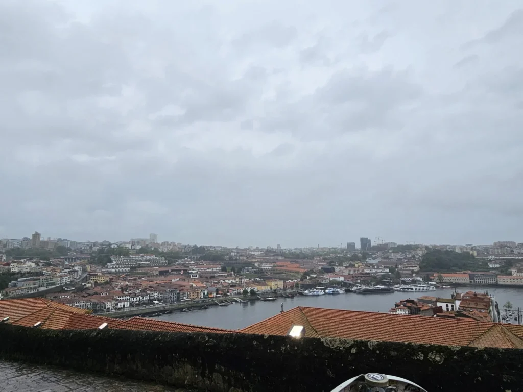 Cruising with Danny and Peter, Holland America Line, Nieuw Statendam, Leixoes, Porto, Portugal, Rainy Adventure | A vibrant collage capturing a rainy day adventure in Porto, Portugal, from the Holland America Line’s Nieuw Statendam cruise. The scene includes a colorful tuk-tuk navigating Porto’s wet, cobblestone streets with historic buildings in the background, the iconic Dom Luís I Bridge spanning the Douro River under gray skies, the majestic Porto Cathedral with its Gothic facade glistening in the rain, and the intricate blue-and-white azulejo tiles of São Bento Station’s atrium. Onboard, a beautifully plated dish from Tamarind restaurant showcases exotic flavors, while the lively Lido Fun Fair on the Lido Midship deck features children enjoying carnival games under a retractable roof, with colorful decorations and cotton candy adding festive cheer.