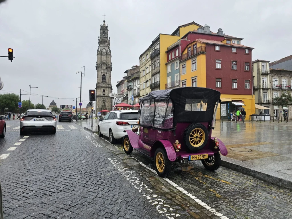 Cruising with Danny and Peter, Holland America Line, Nieuw Statendam, Leixoes, Porto, Portugal, Rainy Adventure | A vibrant collage capturing a rainy day adventure in Porto, Portugal, from the Holland America Line’s Nieuw Statendam cruise. The scene includes a colorful tuk-tuk navigating Porto’s wet, cobblestone streets with historic buildings in the background, the iconic Dom Luís I Bridge spanning the Douro River under gray skies, the majestic Porto Cathedral with its Gothic facade glistening in the rain, and the intricate blue-and-white azulejo tiles of São Bento Station’s atrium. Onboard, a beautifully plated dish from Tamarind restaurant showcases exotic flavors, while the lively Lido Fun Fair on the Lido Midship deck features children enjoying carnival games under a retractable roof, with colorful decorations and cotton candy adding festive cheer.