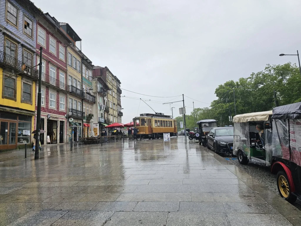 Cruising with Danny and Peter, Holland America Line, Nieuw Statendam, Leixoes, Porto, Portugal, Rainy Adventure | A vibrant collage capturing a rainy day adventure in Porto, Portugal, from the Holland America Line’s Nieuw Statendam cruise. The scene includes a colorful tuk-tuk navigating Porto’s wet, cobblestone streets with historic buildings in the background, the iconic Dom Luís I Bridge spanning the Douro River under gray skies, the majestic Porto Cathedral with its Gothic facade glistening in the rain, and the intricate blue-and-white azulejo tiles of São Bento Station’s atrium. Onboard, a beautifully plated dish from Tamarind restaurant showcases exotic flavors, while the lively Lido Fun Fair on the Lido Midship deck features children enjoying carnival games under a retractable roof, with colorful decorations and cotton candy adding festive cheer.