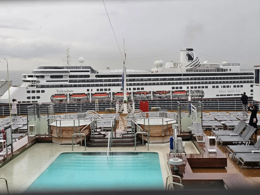 Cruising with Danny and Peter, Holland America Line, Nieuw Statendam, Leixoes, Porto, Portugal, Rainy Adventure | A vibrant collage capturing a rainy day adventure in Porto, Portugal, from the Holland America Line’s Nieuw Statendam cruise. The scene includes a colorful tuk-tuk navigating Porto’s wet, cobblestone streets with historic buildings in the background, the iconic Dom Luís I Bridge spanning the Douro River under gray skies, the majestic Porto Cathedral with its Gothic facade glistening in the rain, and the intricate blue-and-white azulejo tiles of São Bento Station’s atrium. Onboard, a beautifully plated dish from Tamarind restaurant showcases exotic flavors, while the lively Lido Fun Fair on the Lido Midship deck features children enjoying carnival games under a retractable roof, with colorful decorations and cotton candy adding festive cheer.