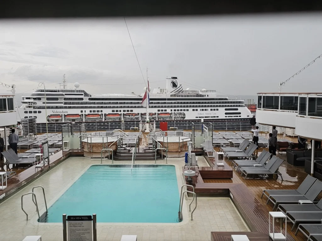 Cruising with Danny and Peter, Holland America Line, Nieuw Statendam, Leixoes, Porto, Portugal, Rainy Adventure | A vibrant collage capturing a rainy day adventure in Porto, Portugal, from the Holland America Line’s Nieuw Statendam cruise. The scene includes a colorful tuk-tuk navigating Porto’s wet, cobblestone streets with historic buildings in the background, the iconic Dom Luís I Bridge spanning the Douro River under gray skies, the majestic Porto Cathedral with its Gothic facade glistening in the rain, and the intricate blue-and-white azulejo tiles of São Bento Station’s atrium. Onboard, a beautifully plated dish from Tamarind restaurant showcases exotic flavors, while the lively Lido Fun Fair on the Lido Midship deck features children enjoying carnival games under a retractable roof, with colorful decorations and cotton candy adding festive cheer.