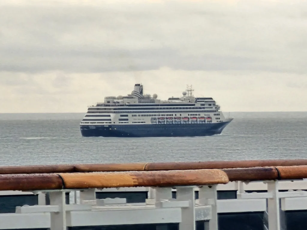 Cruising with Danny and Peter, Holland America Line, Nieuw Statendam, Leixoes, Porto, Portugal, Rainy Adventure | A vibrant collage capturing a rainy day adventure in Porto, Portugal, from the Holland America Line’s Nieuw Statendam cruise. The scene includes a colorful tuk-tuk navigating Porto’s wet, cobblestone streets with historic buildings in the background, the iconic Dom Luís I Bridge spanning the Douro River under gray skies, the majestic Porto Cathedral with its Gothic facade glistening in the rain, and the intricate blue-and-white azulejo tiles of São Bento Station’s atrium. Onboard, a beautifully plated dish from Tamarind restaurant showcases exotic flavors, while the lively Lido Fun Fair on the Lido Midship deck features children enjoying carnival games under a retractable roof, with colorful decorations and cotton candy adding festive cheer.