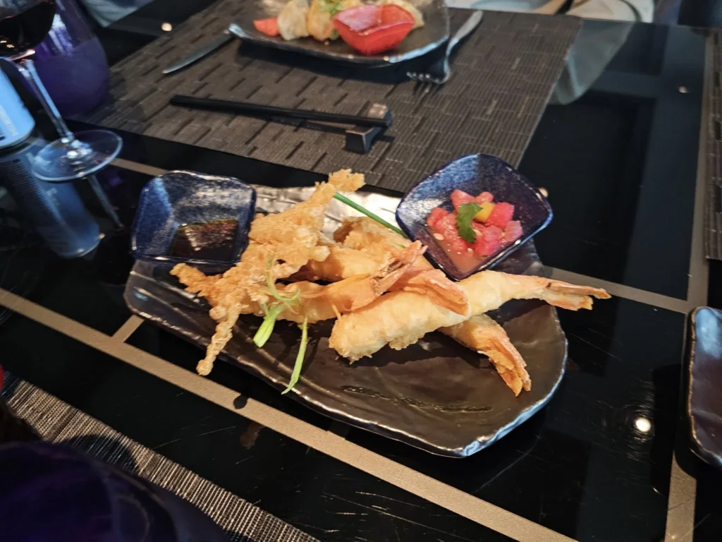 Cruising with Danny and Peter, Holland America Line, Nieuw Statendam, Leixoes, Porto, Portugal, Rainy Adventure | A vibrant collage capturing a rainy day adventure in Porto, Portugal, from the Holland America Line’s Nieuw Statendam cruise. The scene includes a colorful tuk-tuk navigating Porto’s wet, cobblestone streets with historic buildings in the background, the iconic Dom Luís I Bridge spanning the Douro River under gray skies, the majestic Porto Cathedral with its Gothic facade glistening in the rain, and the intricate blue-and-white azulejo tiles of São Bento Station’s atrium. Onboard, a beautifully plated dish from Tamarind restaurant showcases exotic flavors, while the lively Lido Fun Fair on the Lido Midship deck features children enjoying carnival games under a retractable roof, with colorful decorations and cotton candy adding festive cheer.