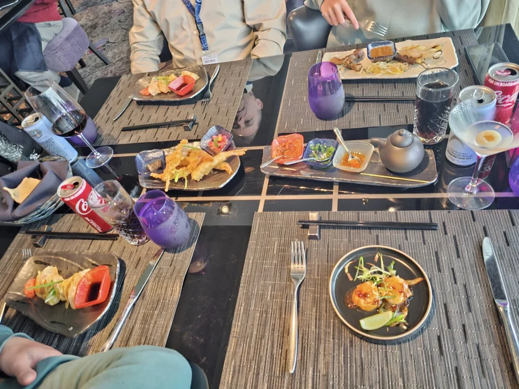 Cruising with Danny and Peter, Holland America Line, Nieuw Statendam, Leixoes, Porto, Portugal, Rainy Adventure | A vibrant collage capturing a rainy day adventure in Porto, Portugal, from the Holland America Line’s Nieuw Statendam cruise. The scene includes a colorful tuk-tuk navigating Porto’s wet, cobblestone streets with historic buildings in the background, the iconic Dom Luís I Bridge spanning the Douro River under gray skies, the majestic Porto Cathedral with its Gothic facade glistening in the rain, and the intricate blue-and-white azulejo tiles of São Bento Station’s atrium. Onboard, a beautifully plated dish from Tamarind restaurant showcases exotic flavors, while the lively Lido Fun Fair on the Lido Midship deck features children enjoying carnival games under a retractable roof, with colorful decorations and cotton candy adding festive cheer.