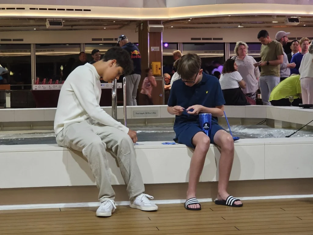 Cruising with Danny and Peter, Holland America Line, Nieuw Statendam, Leixoes, Porto, Portugal, Rainy Adventure | A vibrant collage capturing a rainy day adventure in Porto, Portugal, from the Holland America Line’s Nieuw Statendam cruise. The scene includes a colorful tuk-tuk navigating Porto’s wet, cobblestone streets with historic buildings in the background, the iconic Dom Luís I Bridge spanning the Douro River under gray skies, the majestic Porto Cathedral with its Gothic facade glistening in the rain, and the intricate blue-and-white azulejo tiles of São Bento Station’s atrium. Onboard, a beautifully plated dish from Tamarind restaurant showcases exotic flavors, while the lively Lido Fun Fair on the Lido Midship deck features children enjoying carnival games under a retractable roof, with colorful decorations and cotton candy adding festive cheer.