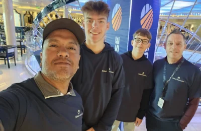 Cruising with Danny and Peter, Holland America Line, Nieuw Statendam, Biscay Bliss Sea Day | A vibrant collage capturing a sea day aboard Holland America Line’s Nieuw Statendam in the Bay of Biscay. The scene includes a pod of dolphins leaping gracefully through shimmering blue waves alongside the ship, their sleek bodies catching the sunlight. Passengers walk energetically on the sunlit deck during a charity event, with the vast ocean horizon stretching behind them. The elegant interior of Rudi’s Sel de Mer restaurant features a beautifully set table with a plate of seared scallops and a chocolate soufflé, illuminated by warm lighting. The World Stage theater glows with a large LED screen displaying Dover’s white cliffs, as the audience listens attentively to a port talk. A couple poses for a photoshoot on deck at sunset, framed by the golden glow of the Bay of Biscay’s horizon, with the ship’s sleek railings in the foreground.