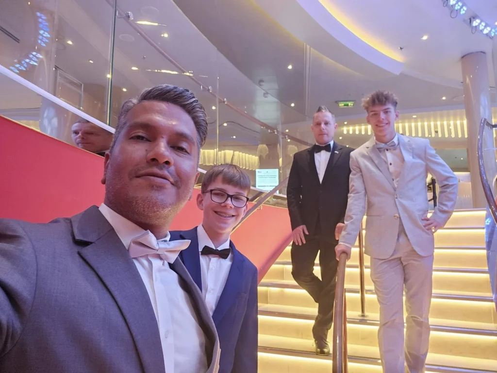 Cruising with Danny and Peter, Holland America Line, Nieuw Statendam, Biscay Bliss Sea Day | A vibrant collage capturing a sea day aboard Holland America Line’s Nieuw Statendam in the Bay of Biscay. The scene includes a pod of dolphins leaping gracefully through shimmering blue waves alongside the ship, their sleek bodies catching the sunlight. Passengers walk energetically on the sunlit deck during a charity event, with the vast ocean horizon stretching behind them. The elegant interior of Rudi’s Sel de Mer restaurant features a beautifully set table with a plate of seared scallops and a chocolate soufflé, illuminated by warm lighting. The World Stage theater glows with a large LED screen displaying Dover’s white cliffs, as the audience listens attentively to a port talk. A couple poses for a photoshoot on deck at sunset, framed by the golden glow of the Bay of Biscay’s horizon, with the ship’s sleek railings in the foreground.