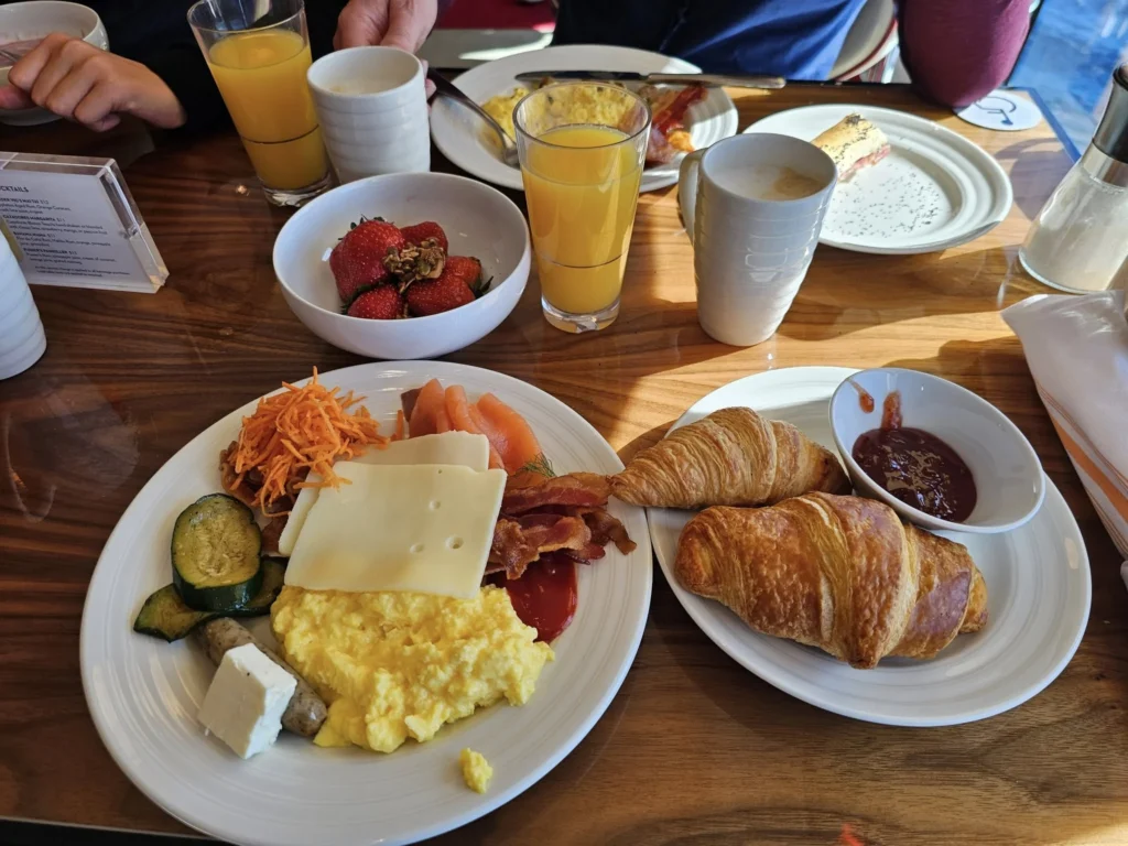 Cruising with Danny and Peter, Holland America Line, Nieuw Statendam, Biscay Bliss Sea Day | A vibrant collage capturing a sea day aboard Holland America Line’s Nieuw Statendam in the Bay of Biscay. The scene includes a pod of dolphins leaping gracefully through shimmering blue waves alongside the ship, their sleek bodies catching the sunlight. Passengers walk energetically on the sunlit deck during a charity event, with the vast ocean horizon stretching behind them. The elegant interior of Rudi’s Sel de Mer restaurant features a beautifully set table with a plate of seared scallops and a chocolate soufflé, illuminated by warm lighting. The World Stage theater glows with a large LED screen displaying Dover’s white cliffs, as the audience listens attentively to a port talk. A couple poses for a photoshoot on deck at sunset, framed by the golden glow of the Bay of Biscay’s horizon, with the ship’s sleek railings in the foreground.