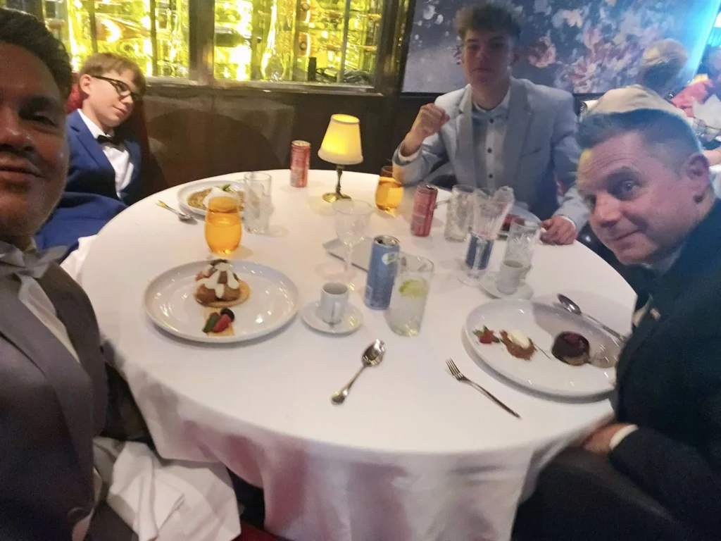 Cruising with Danny and Peter, Holland America Line, Nieuw Statendam, Biscay Bliss Sea Day | A vibrant collage capturing a sea day aboard Holland America Line’s Nieuw Statendam in the Bay of Biscay. The scene includes a pod of dolphins leaping gracefully through shimmering blue waves alongside the ship, their sleek bodies catching the sunlight. Passengers walk energetically on the sunlit deck during a charity event, with the vast ocean horizon stretching behind them. The elegant interior of Rudi’s Sel de Mer restaurant features a beautifully set table with a plate of seared scallops and a chocolate soufflé, illuminated by warm lighting. The World Stage theater glows with a large LED screen displaying Dover’s white cliffs, as the audience listens attentively to a port talk. A couple poses for a photoshoot on deck at sunset, framed by the golden glow of the Bay of Biscay’s horizon, with the ship’s sleek railings in the foreground.