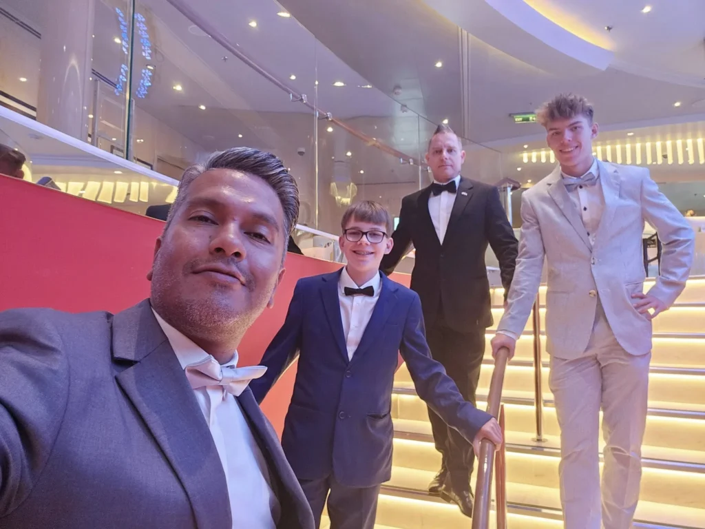 Cruising with Danny and Peter, Holland America Line, Nieuw Statendam, Biscay Bliss Sea Day | A vibrant collage capturing a sea day aboard Holland America Line’s Nieuw Statendam in the Bay of Biscay. The scene includes a pod of dolphins leaping gracefully through shimmering blue waves alongside the ship, their sleek bodies catching the sunlight. Passengers walk energetically on the sunlit deck during a charity event, with the vast ocean horizon stretching behind them. The elegant interior of Rudi’s Sel de Mer restaurant features a beautifully set table with a plate of seared scallops and a chocolate soufflé, illuminated by warm lighting. The World Stage theater glows with a large LED screen displaying Dover’s white cliffs, as the audience listens attentively to a port talk. A couple poses for a photoshoot on deck at sunset, framed by the golden glow of the Bay of Biscay’s horizon, with the ship’s sleek railings in the foreground.