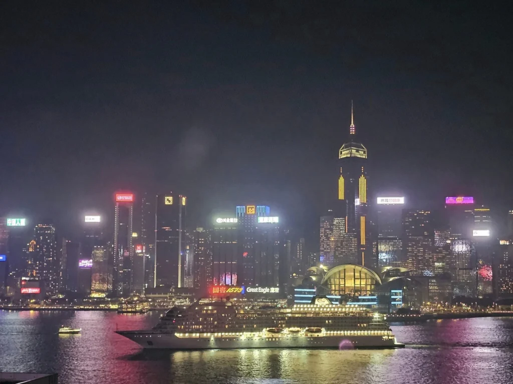 Cruising with Danny and Peter, Holland America Line, Westerdam, Hong Kong, China, Hong Kong Travel Guide: 10 Irresistible Gems | Panoramic Hong Kong Skyline Views from Sky100 Observation Deck showcasing Victoria Harbour and glittering skyscrapers at dusk, paired with a vibrant Temple Street Market scene featuring colorful stalls offering Hong Kong Street Food like dim sum, egg tarts, wonton noodles, and crispy fish balls in a bustling Hong Kong Night Markets atmosphere, alongside a scenic Tsim Sha Tsui Promenade view of Victoria Harbour with illuminated Hong Kong Skyline Views perfect for Hong Kong Tourism evenings, and the Holland America Line’s Westerdam docked in Hong Kong, marking the end of a Cruise Travel Hong Kong journey with Hong Kong Attractions in the background.