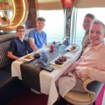 Cruising with Danny and Peter, Holland America Line, Nieuw Statendam, English Channel Sea Day | A montage of a sea day on Holland America’s Nieuw Statendam sailing the English Channel: calm waters meet Dover’s distant white cliffs from a balcony; Sven and Liam play pickleball on a sunlit deck with cheering crowds and a blue sea backdrop; vibrant cakes—chocolate, fruit, and cream-topped—fill the Lido Market as crew serve slices; a candlelit Canaletto table holds Italian dishes in a cozy, rustic dining room.