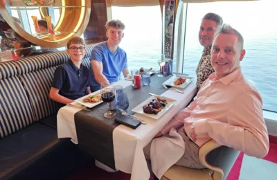 Cruising with Danny and Peter, Holland America Line, Nieuw Statendam, English Channel Sea Day | A montage of a sea day on Holland America’s Nieuw Statendam sailing the English Channel: calm waters meet Dover’s distant white cliffs from a balcony; Sven and Liam play pickleball on a sunlit deck with cheering crowds and a blue sea backdrop; vibrant cakes—chocolate, fruit, and cream-topped—fill the Lido Market as crew serve slices; a candlelit Canaletto table holds Italian dishes in a cozy, rustic dining room.