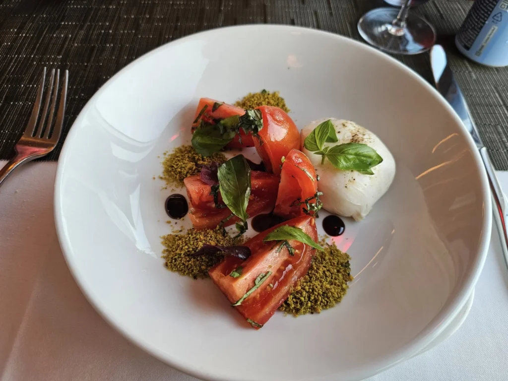 Cruising with Danny and Peter, Holland America Line, Nieuw Statendam, English Channel Sea Day | A montage of a sea day on Holland America’s Nieuw Statendam sailing the English Channel: calm waters meet Dover’s distant white cliffs from a balcony; Sven and Liam play pickleball on a sunlit deck with cheering crowds and a blue sea backdrop; vibrant cakes—chocolate, fruit, and cream-topped—fill the Lido Market as crew serve slices; a candlelit Canaletto table holds Italian dishes in a cozy, rustic dining room.