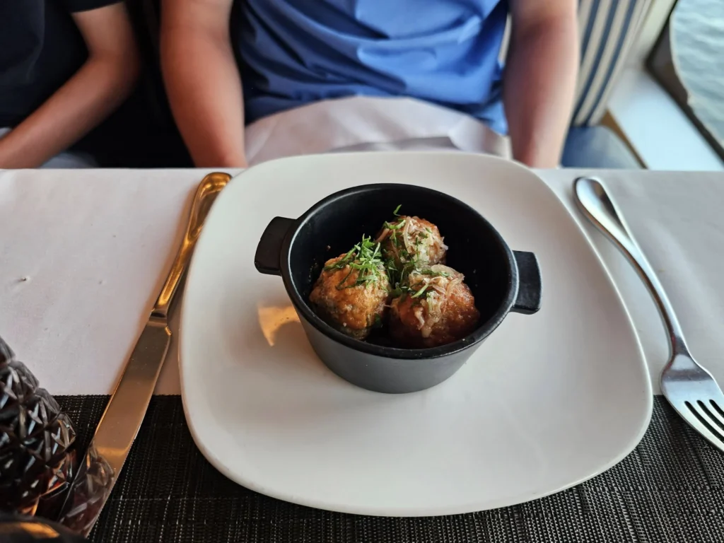 Cruising with Danny and Peter, Holland America Line, Nieuw Statendam, English Channel Sea Day | A montage of a sea day on Holland America’s Nieuw Statendam sailing the English Channel: calm waters meet Dover’s distant white cliffs from a balcony; Sven and Liam play pickleball on a sunlit deck with cheering crowds and a blue sea backdrop; vibrant cakes—chocolate, fruit, and cream-topped—fill the Lido Market as crew serve slices; a candlelit Canaletto table holds Italian dishes in a cozy, rustic dining room.