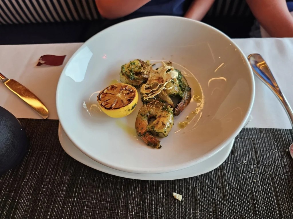 Cruising with Danny and Peter, Holland America Line, Nieuw Statendam, English Channel Sea Day | A montage of a sea day on Holland America’s Nieuw Statendam sailing the English Channel: calm waters meet Dover’s distant white cliffs from a balcony; Sven and Liam play pickleball on a sunlit deck with cheering crowds and a blue sea backdrop; vibrant cakes—chocolate, fruit, and cream-topped—fill the Lido Market as crew serve slices; a candlelit Canaletto table holds Italian dishes in a cozy, rustic dining room.