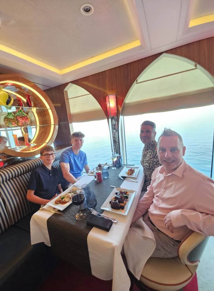 Cruising with Danny and Peter, Holland America Line, Nieuw Statendam, English Channel Sea Day | A montage of a sea day on Holland America’s Nieuw Statendam sailing the English Channel: calm waters meet Dover’s distant white cliffs from a balcony; Sven and Liam play pickleball on a sunlit deck with cheering crowds and a blue sea backdrop; vibrant cakes—chocolate, fruit, and cream-topped—fill the Lido Market as crew serve slices; a candlelit Canaletto table holds Italian dishes in a cozy, rustic dining room.