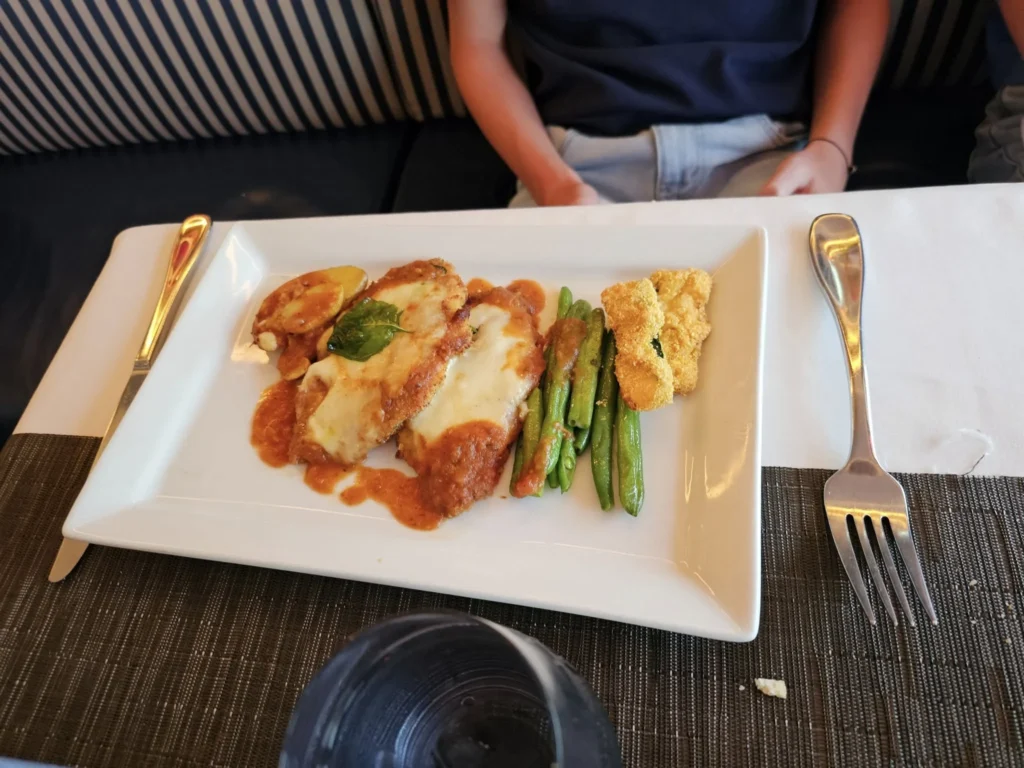 Cruising with Danny and Peter, Holland America Line, Nieuw Statendam, English Channel Sea Day | A montage of a sea day on Holland America’s Nieuw Statendam sailing the English Channel: calm waters meet Dover’s distant white cliffs from a balcony; Sven and Liam play pickleball on a sunlit deck with cheering crowds and a blue sea backdrop; vibrant cakes—chocolate, fruit, and cream-topped—fill the Lido Market as crew serve slices; a candlelit Canaletto table holds Italian dishes in a cozy, rustic dining room.