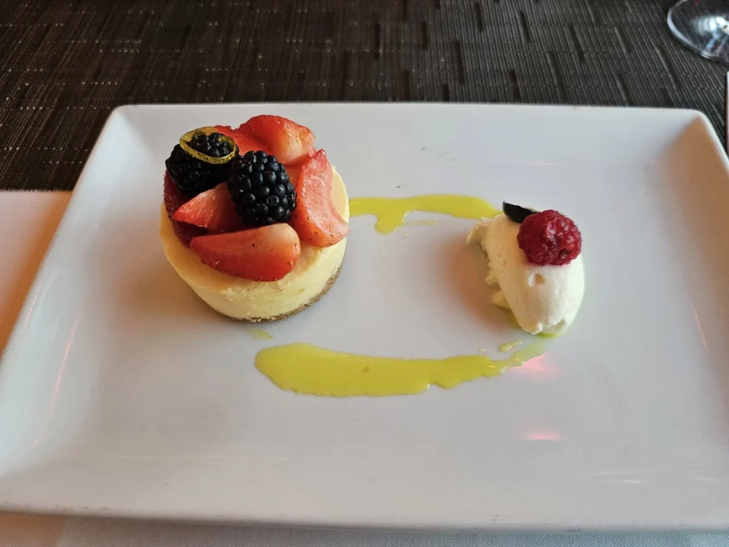 Cruising with Danny and Peter, Holland America Line, Nieuw Statendam, English Channel Sea Day | A montage of a sea day on Holland America’s Nieuw Statendam sailing the English Channel: calm waters meet Dover’s distant white cliffs from a balcony; Sven and Liam play pickleball on a sunlit deck with cheering crowds and a blue sea backdrop; vibrant cakes—chocolate, fruit, and cream-topped—fill the Lido Market as crew serve slices; a candlelit Canaletto table holds Italian dishes in a cozy, rustic dining room.