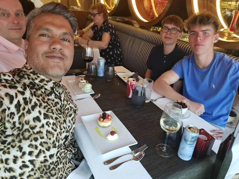 Cruising with Danny and Peter, Holland America Line, Nieuw Statendam, English Channel Sea Day | A montage of a sea day on Holland America’s Nieuw Statendam sailing the English Channel: calm waters meet Dover’s distant white cliffs from a balcony; Sven and Liam play pickleball on a sunlit deck with cheering crowds and a blue sea backdrop; vibrant cakes—chocolate, fruit, and cream-topped—fill the Lido Market as crew serve slices; a candlelit Canaletto table holds Italian dishes in a cozy, rustic dining room.