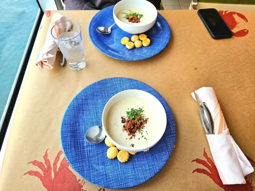 Cruising with Danny and Peter, Holland America Line, Nieuw Statendam, Palma de Mallorca, Spain | Scenic coastal drive in Mallorca during the Palma de Mallorca Sunset Tour, featuring rugged cliffs and azure waters. Historic Palma Cathedral with Gothic architecture is also highlighted. The luxurious seafood feast aboard MS Nieuw Statendam includes lobster, shrimp, and crab, complemented by a stunning Mediterranean sunset with pink and gold hues in the sky.