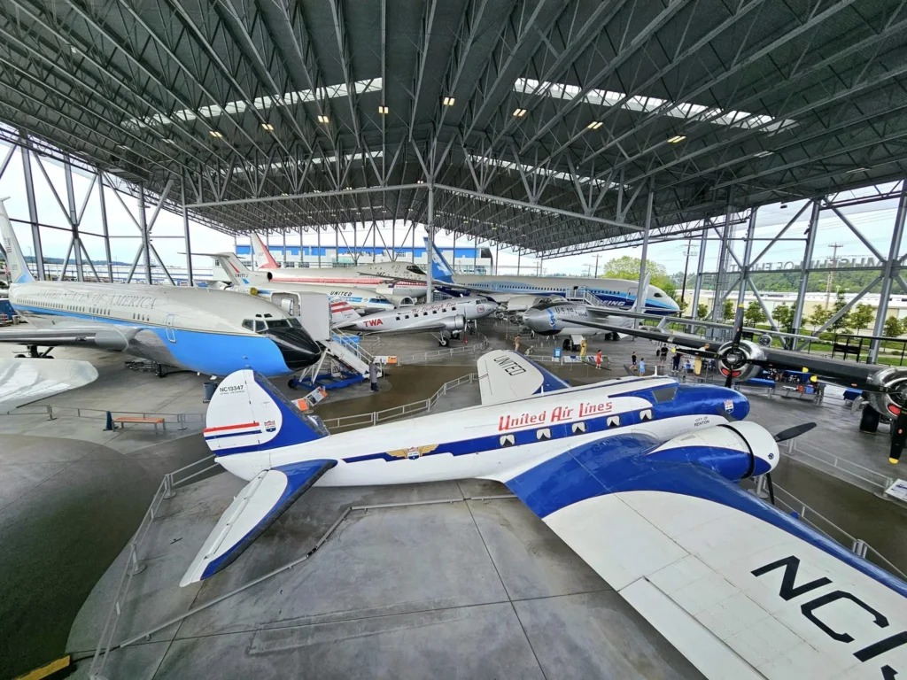 Cruising with Danny and Peter, Holland America Line, Westerdam, Seattle, Washington, United States, Day Trip Waterfalls History | A vibrant collage captures a day in Seattle’s Pacific Northwest Waterfalls Tour, showcasing Pike Place Market’s bustling scene with fishmongers tossing salmon and colorful flower stalls under the iconic red neon sign, set against Puget Sound’s waterfront; Twin Falls cascading over mossy cliffs into a misty pool, surrounded by old-growth evergreens in Olallie State Park, with sunlight filtering through the canopy; North Bend’s retro Twin Peaks diner with its glowing neon sign and quaint main street, framed by rolling hills and the Cascade Mountains; the majestic 270-foot Snoqualmie Falls roaring into a misty pool, with rainbows shimmering in the sunlight and a wooden viewing platform overlooking the lush Snoqualmie Valley; Snoqualmie’s historic district, featuring the Northwest Railway Museum’s vintage locomotives and charming shops lined with old-fashioned street lamps; Borst Lake’s serene waters reflecting Mount Si’s snow-capped peak, with a heron at the edge and evergreen forests under a soft morning mist; and the Museum of Flight’s sleek Concorde and Air Force One jets displayed in a spacious hangar, alongside interactive simulators and a replica of the International Space Station, showcasing Seattle’s aviation heritage.