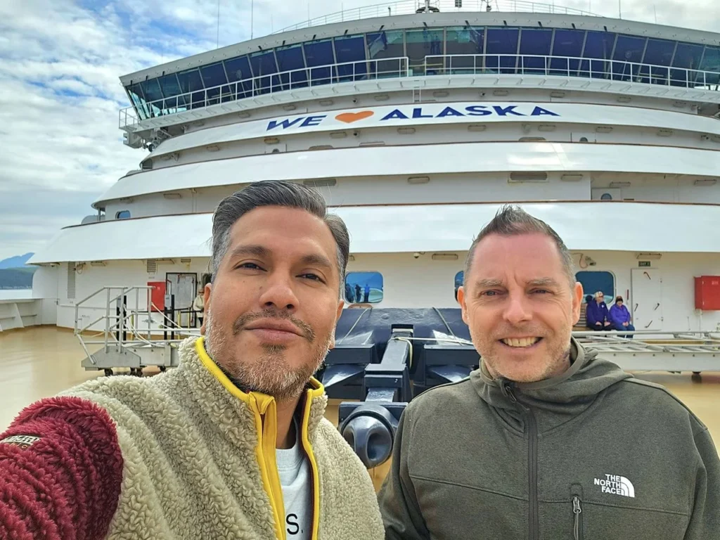 Cruising with Danny and Peter, Holland America Line, Westerdam, Inside Passage, Alaska, United States | Westerdam luxury cruise ship sailing through the Inside Passage, with majestic glaciers and dramatic landscapes in view. The image features an elegant stateroom with a spacious veranda, offering panoramic scenery, and highlights gourmet dining and an informative lecture by onboard naturalists, showcasing the comprehensive luxury and educational experience of the cruise.