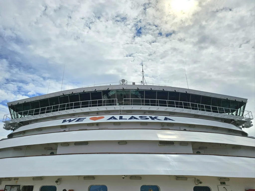 Cruising with Danny and Peter, Holland America Line, Westerdam, Inside Passage, Alaska, United States | Westerdam luxury cruise ship sailing through the Inside Passage, with majestic glaciers and dramatic landscapes in view. The image features an elegant stateroom with a spacious veranda, offering panoramic scenery, and highlights gourmet dining and an informative lecture by onboard naturalists, showcasing the comprehensive luxury and educational experience of the cruise.