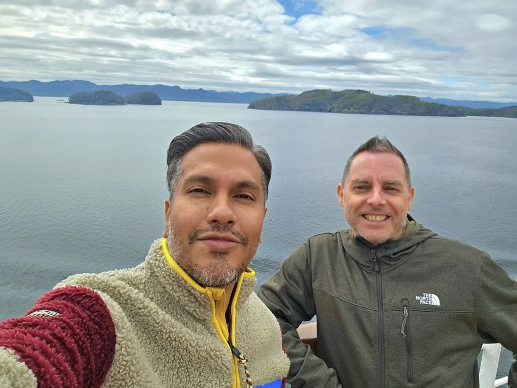 Cruising with Danny and Peter, Holland America Line, Westerdam, Inside Passage, Alaska, United States | Westerdam luxury cruise ship sailing through the Inside Passage, with majestic glaciers and dramatic landscapes in view. The image features an elegant stateroom with a spacious veranda, offering panoramic scenery, and highlights gourmet dining and an informative lecture by onboard naturalists, showcasing the comprehensive luxury and educational experience of the cruise.