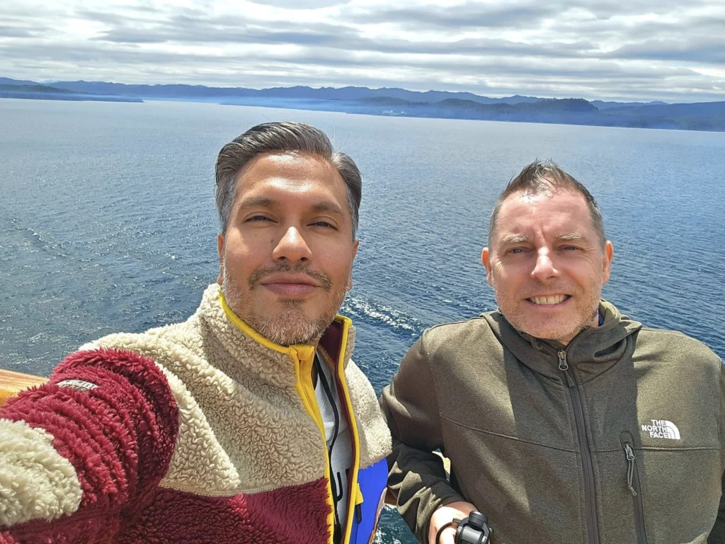 Cruising with Danny and Peter, Holland America Line, Westerdam, Inside Passage, Alaska, United States | Westerdam luxury cruise ship sailing through the Inside Passage, with majestic glaciers and dramatic landscapes in view. The image features an elegant stateroom with a spacious veranda, offering panoramic scenery, and highlights gourmet dining and an informative lecture by onboard naturalists, showcasing the comprehensive luxury and educational experience of the cruise.